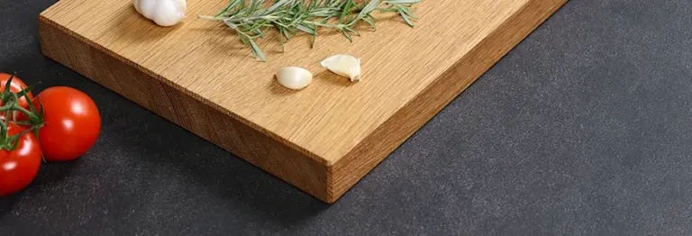 Handgefertigtes Schneidebrett aus Eiche mit gefasten Kanten, dekoriert mit Knoblauch, Tomaten und Rosmarin