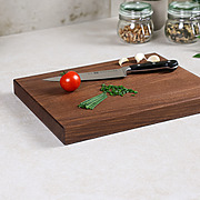 Schneidebrett aus dunklem Nussbaumholz von links schräg mit Messer, Tomaten und Küchenkräutern