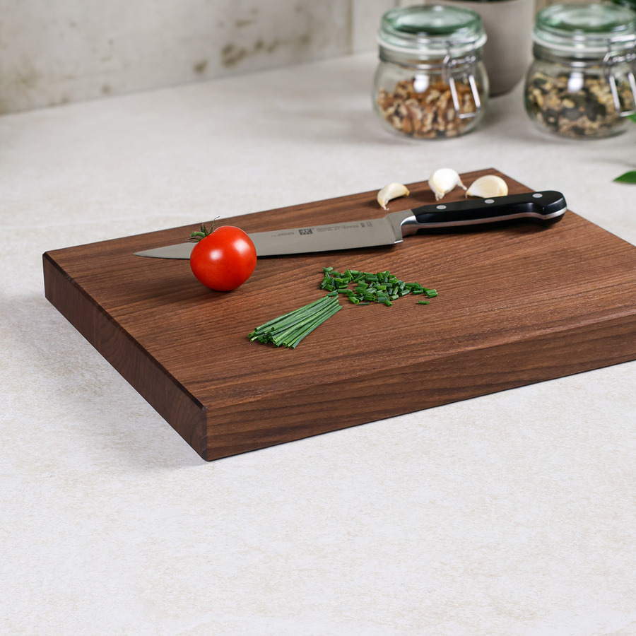 schneidebrett-amerikanischer-nussbaum-das-edle-links-schraeg Schneidebrett aus dunklem Nussbaumholz von links schräg mit Messer, Tomaten und Küchenkräutern